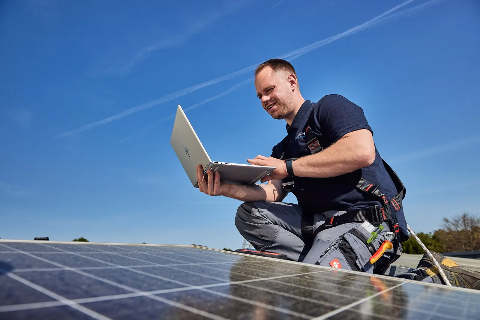 Monteur mit Laptop auf einem Dach neben Solarmodulen