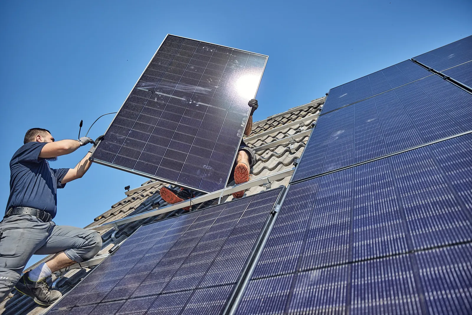 Monteur trägt ein Photovoltaikmodul über das Dach